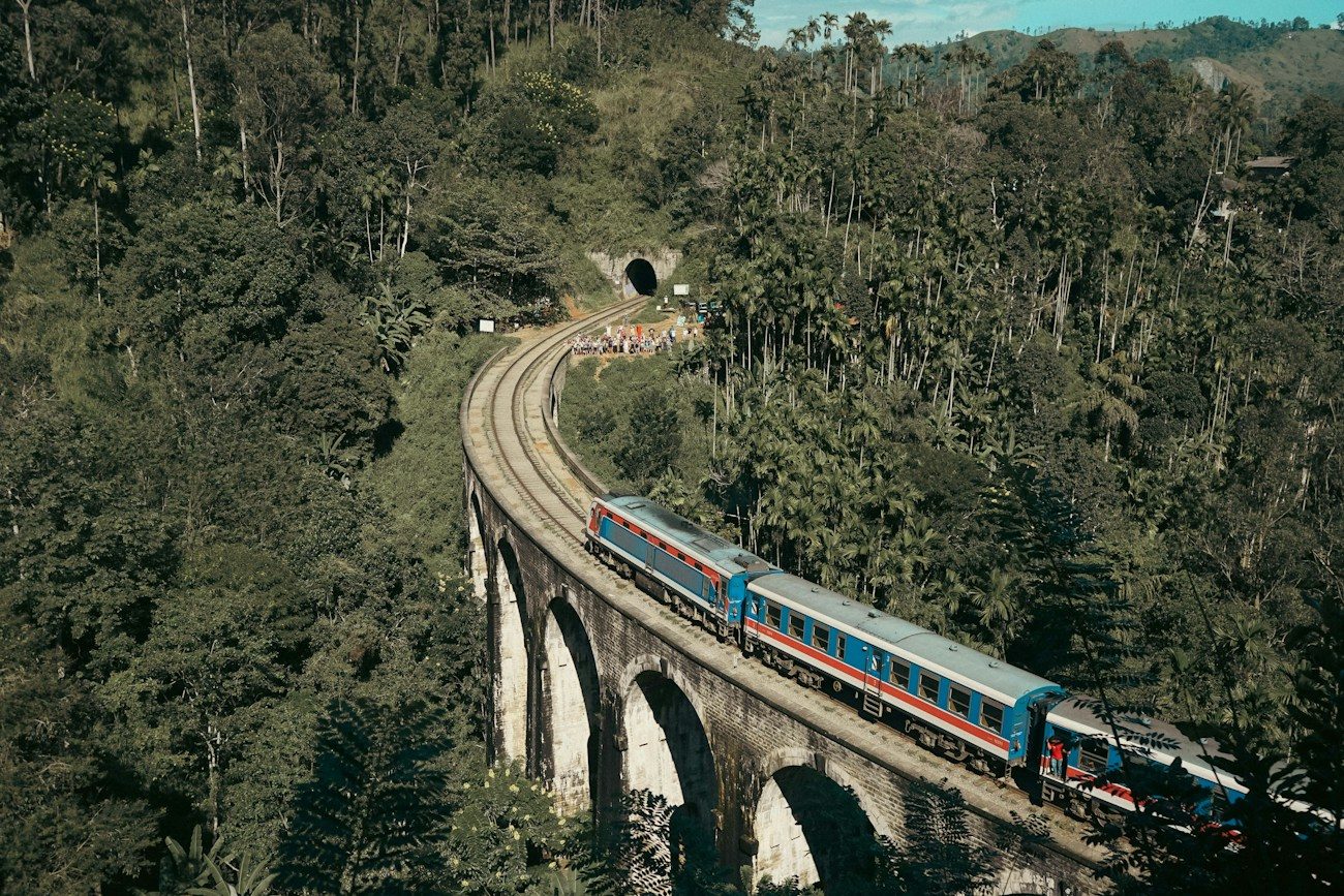 A train crossing the Nine Arch Bridge among the green hills of Ella